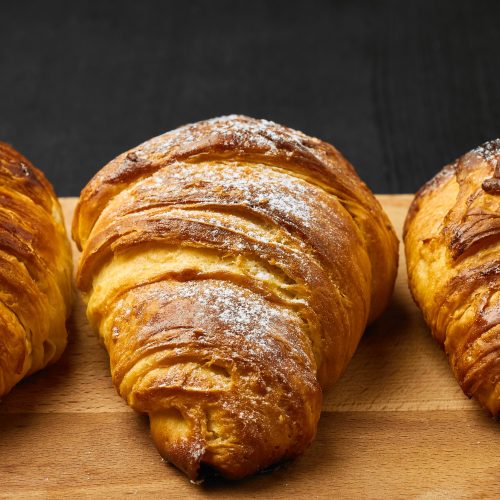 Three croissants with sugar powder on a wooden desk on a black background. Homemade baking concept