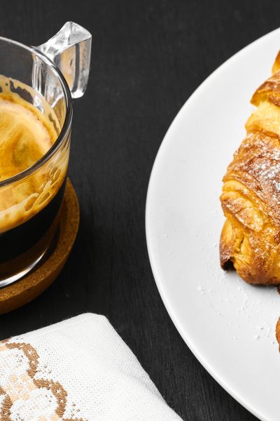 A cup of coffee, buttery croissants and cotton towel on a black background. Idea of breakfast